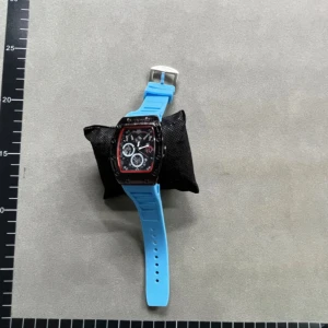 Richard Mille blå sportklocka - Säljer en Richard Mille klocka med sportig vibe och blått syntetarmband. Klockan har en rektangulär svart urtavla med röda detaljer och flera små visare. Snyggt silverfärgat spänne och cool box medföljer. Perfekt för dig som gillar statement-accessoarer.