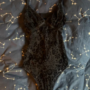 Svart blommig body - Supersnygg svart body från Cubus i storlek XS med blommigt mönster och öppen rygg. Bodynhar smala axelband och ett spänne i ryggen. Helt perfekt för en utekväll på stan.