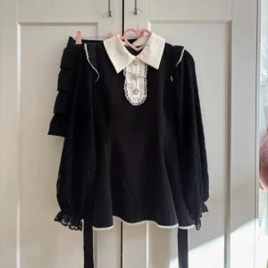 Svart och vit klänning från Honey Cinnamon - Supersöt svart set up med vit krage och dekorativa pärlknappar framtill. Klänningen har långa spetsärmar, volangdetaljer vid axlarna och spetskant längs krage och nederkant.  Perfekt för jirai kei