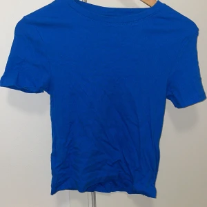 Blå ribbad topp från New Yorker - Snygg blå ribbad topp från FSBN Sister i storlek M. Modellen har rund hals och korta ärmar, perfekt för dig som gillar enkel och stilren design. Materialet är mjukt och stretchigt bomull som sitter skönt mot kroppen.