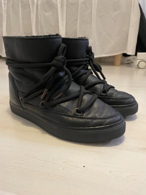 Svarta Inuikii boots med snörning - Säljer ett par svarta Inuikii boots med grov snörning och rund tå. Skorna är tillverkade i skinn och har en platt sula med mönstrad undersida. Insidan är fodrad med mjukt material för extra värme. Perfekta för kalla dagar och har en cool, chunky look. Priset kan diskuteras!!💕