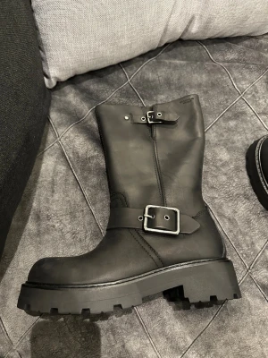 Svarta boots från Vagabond med spännen - Säljer ett par svarta boots från Vagabond i skinn med grov platt sula och två metallspännen. Modellen har rund tå och robust yttersula med tydligt mönster för extra grepp. Perfekt för dig som gillar chunky och stilrena skor.