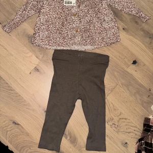 Blommig skjorta med knappar, H&M Set Storlek 68 - Söt skjorta från H&M med små bruna blommor på vit botten. Skjortan har klassisk krage, långa ärmar och knappar framtill. Perfekt för dig som gillar detaljer och mönster. Materialet är mjuk bomull som känns skönt mot huden.Fint set med en blus med blommor och ett par leggings. 🎁 