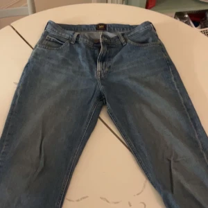 Blå jeans från Lee W30 L32 - Snygga klassiska blå jeans från Lee i modellen West. Jeansen har fem fickor, rak passform och normal midja. Tillverkade i slitstarkt denim med Lee-logga på bakfickan och läderpatch vid linningen. Perfekt för dig som gillar tidlös stil.