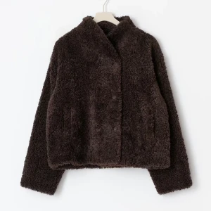 Mörkbrun teddyjacka med knappar - Mysig mörkbrun teddyjacka med klassisk krage och knäppning framtill. Jackan har en fluffig och mjuk yta som ger en cool och avslappnad vibe. Perfekt för dig som gillar att hålla dig varm och samtidigt se trendig ut.