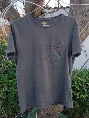 Mörkgrå t-shirt Polo Ralph Lauren S - Mörkgrå t-shirt från Polo Ralph Lauren i storlek S. Klassisk modell med rund hals, korta ärmar och bröstficka med rosa broderad logga. Tillverkad i mjuk bomull för en skön känsla. Perfekt basic med stilren look.