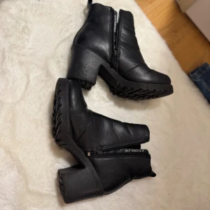 Svarta chelsea boots med klack - Snygga svarta chelsea boots med grov sula och stabil klack. Skorna är tillverkade i skinn och har elastiska paneler på sidorna samt dragkedja för enkel påtagning. Rund tå och platt sula framtill ger en cool och robust look.