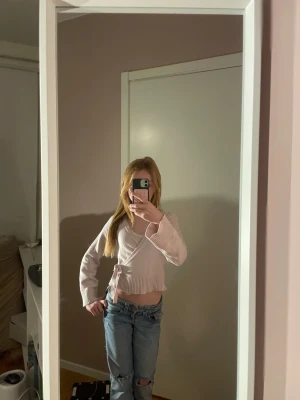 Ljusrosa omlott kofta med knyt - Superfin ljusrosa omlott kofta från Gina tricot med knyt i midjan och breda ribbade muddar. Croppad modell med långärmade ärmar och mjukt stickat material som är perfekt för lager-på-lager. Snygg att matcha med jeans eller kjol.