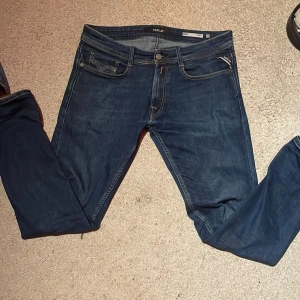 Replay blå jeans med raka ben - Snygga mörkblå jeans från Replay med klassisk femficksdesign och raka ben. Jeansen har kontrastsömmar, läderpatch bak och detaljerad fickdesign. Perfekt för dig som gillar stilrena och tidlösa jeans med coola detaljer.