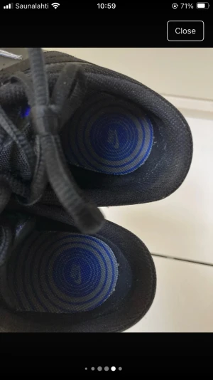 Svarta Nike sneakers med blå detaljer - Nike sneakers i svart med blå detaljer och vit swoosh på sidan. Skorna har snörning, rund tå och platt sula. Märket syns tydligt på hälen i blått. Materialet är syntet och textil, vilket gör dem både lätta och bekväma för vardagsbruk.