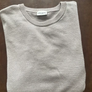 Beige stickad tröja från John Henric - Snygg beige stickad tröja från John Henric i storlek M. Tröjan har rund hals och är tillverkad i marinull som känns skönt mot huden. Perfekt för dig som gillar stilrena och enkla plagg med klassisk look.