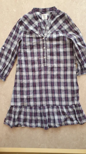 Skjortklänning - Rutig skjortklänning från H&M i blått, vitt och rött. Klänningen har trekvartsärmar med knappdetaljer, knappar framtill och en volang längst ner. Tillverkad i mjuk bomull, perfekt för en chill och avslappnad stil.