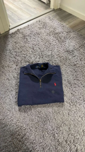 Marinblå half zip tröja Polo Ralph Lauren - Snygg marinblå långärmad tröja från Polo Ralph Lauren med half zip och klassisk röd broderad logga på bröstet. Tröjan är i mjuk bomull och har en stilren krage. Perfekt för dig som gillar enkel och tidlös stil.
