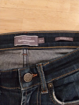 Mörkblå jeans från Dressmann 30/30 - Snygga mörkblå jeans från Dressmann i regular fit med klassisk femficksdesign och kontrastsömmar. Jeansen har raka ben och subtila slitningar för en cool look. Passar dig som gillar enkel och stilren denim.