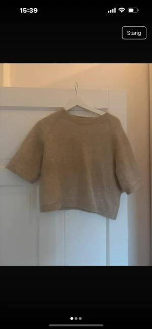 Beige stickad tröja & Other Stories - Kort beige stickad tröja från & Other Stories Stockholm Atelier. Modellen är loose fit med ribbad rund hals och korta ärmar. Perfekt för lager-på-lager och chill stil. Materialet är mjukt och ger en skön känsla mot huden.