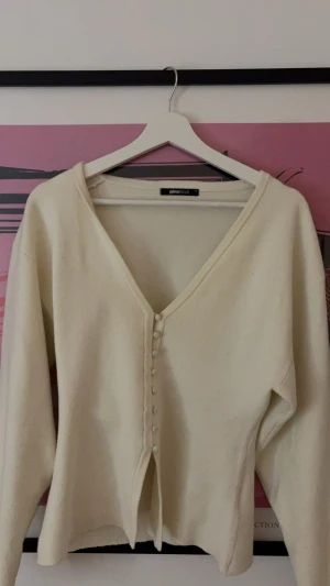Beige kofta med v-ringning Gina Tricot - Snygg beige kofta från Gina Tricot med v-ringad hals och dekorativa knappar framtill. Mjuk och skön, perfekt för lager-på-lager. Långärmad och med en enkel, stilren look som funkar till många outfits. fint skick men lite nopprig.