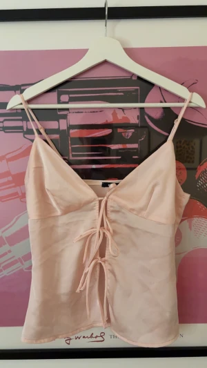 Champagnefärgad linnetopp med snörning - Champagnefärgad linnetopp från Gina Tricot med smala axelband och snygg snörning framtill. Toppen har en mjuk, silkeslen känsla och v-ringad hals. Perfekt för dig som gillar minimalistisk stil med en twist. Säljes i storlek S. Knappast använd.