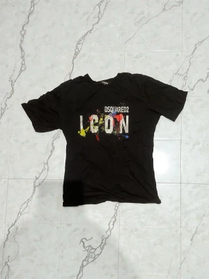 Svart DSQUARED2 ICON t-shirt XL - Svart t-shirt från DSQUARED2 i storlek XL med trycket 'ICON' och färgstänk i gult, rött, blått och vitt på bröstet. Klassisk rund hals och korta ärmar. Materialet är mjuk bomull, perfekt för dig som gillar streetwear med statement. Dessutom så funkar såklart Qr koden. Priset kan såklart förhandlas skicka meddelande om du är intresserad.