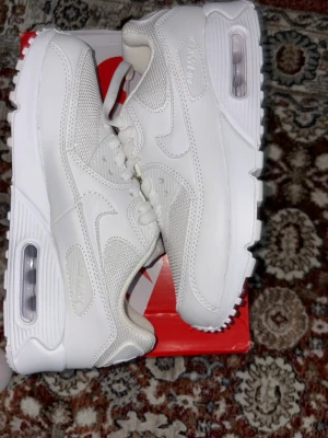 Nike Air Max 90 Triple White sneakers - Nike Air Max 90 Triple White sneakers med klassisk chunky siluett. Helt vita med mesh och skinnpaneler, synlig Air-enhet i sulan och snygga detaljer. Rund tå, snörning och platt sula. Perfekt för dig som gillar cleana och stilrena sneakers.