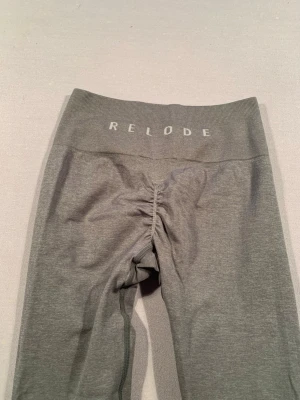 Grå leggings från Relode - Snygga grå leggings från Relode med hög midja och scrunch-detalj bak. Tillverkade i mjukt och stretchigt material som sitter tight och bekvämt. Perfekta för träning eller chill. Diskret logga i midjan och sömlös design för en clean look.