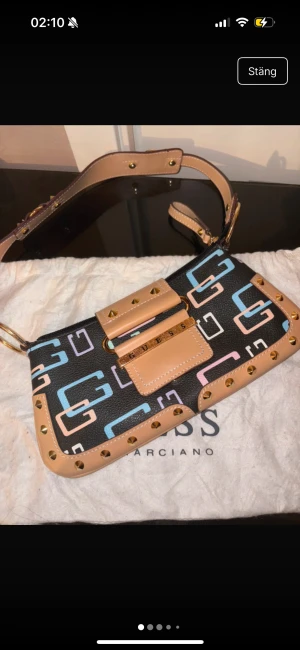 Guess vintage väska - Vintage guess väska, köpt i London vintage butik, kostade 185 punds= 2300kr sek Pris kan alltid diskuteras!💕 material- ej mjuk väska, hårt material och fast. Färger med svart bakgrund och beige detaljer med spikar, en liten inne ficka.