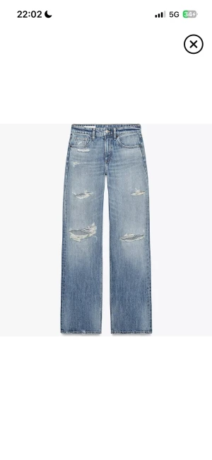 Populära Zara jeans - Säljer ett par blå jeans med coola slitningar och hål på både lår och knän. Jeansen har en rak passform och klassisk femficksdesign. Perfekta för dig som gillar en avslappnad och edgy stil.