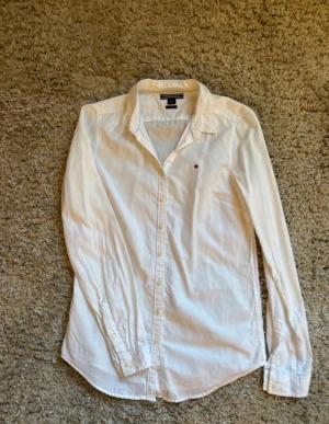 Vit skjorta från Tommy Hilfiger - Vit klassisk skjorta från Tommy Hilfiger med lång ärm och knappar framtill. Fitted storlek s i bomull.