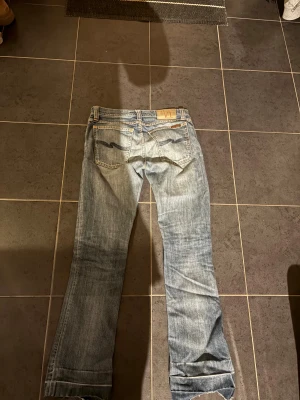 Jeans från Nudie - Säljer ett par ljusblå Jeans med bootcut/slim  passform och slitningar vid knäet. Klassisk femficksmodell med Nudie-logga på bakfickan och låg midja. Säljer då de inte passade mig, hör av er för fler frågor 🫶