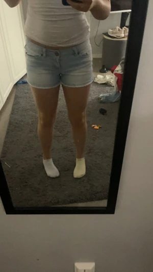 Ljusblå denimshorts med fem fickor - Säljer ett par ljusblå denimshorts med klassisk femficksdesign och knappgylf. Modellen är midwaist och har en normal passform. Perfekt för dig som gillar en enkel och fräsch stil på sommaren. Shortsen har lätt slitning och är tillverkade i bomull. Kan vikas upp om man vill