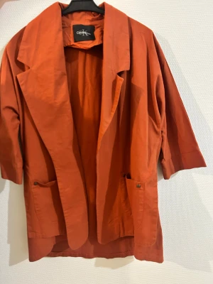 Orange kavaj från Calvin Klein - Snygg orange kavaj från Calvin Klein med breda slag, trekvartsärmar och två framfickor med metallknappar. Jackan är tillverkad i bomull och har en loose passform som ger en chill vibe. Perfekt för dig som vill sticka ut med färg och stil.