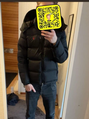 Ralph lauren jacka *Äkta* - Säljer en svart dunjacka från Polo Ralph Lauren i storlek M. Jackan har huva, två sidofickor med dragkedja och en röd Polo-logga på bröstet. Puffad design med quiltade sektioner och hel dragkedja framtill. Perfekt för kalla dagar och riktigt snygg stil. 100% äkta skriv vid minsta fundering, nyskick bara testat 