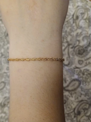 Tunn guldpläterad kedjearmband - Snyggt, elegant och tunt armband med tvinnad kedja i guldpläterad metall. Justerbar längd med flera öglor och en liten rund detalj vid låset. Perfekt för dig som gillar minimalistisk och stilren design.