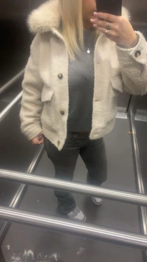 Vit teddyjacka med fluff  - Säljer en fluffig vit teddyjacka med stora fickor och snygga knappar framtill. Jackan har en bred krage och är croppad i modellen, perfekt för dig som gillar en chill och trendig look. Passar dig som vill ha en varm och mysig jacka med cool stil.