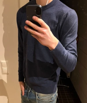 Mörkblå stickad tröja herr - Snygg mörkblå stickad tröja med rund hals och långa ärmar. Passformen är normal och materialet känns mjukt mot huden. Perfekt att matcha med jeans för en clean och enkel look. Tröjan har ribbade muddar vid ärmslut och nederkant.skriv vid funderingar eller frågor