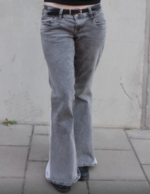 Vega Jeans - Grå jeans med insydda vita kilar, vit spets runt kilarna, tramp stamp i silver och vit ficka med logga.                                                                 Storlek: midja-80cm stuss-92 innebenslängd-80 