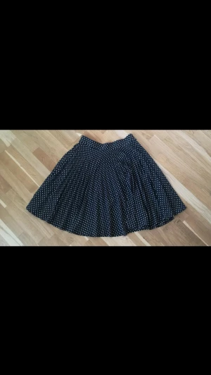 Svart vintage kjol - Svart äkta vintage kjol med vita prickar från Hennes Collection by H&M. Kjolen är i väldigt fint skick. Perfekt för dig som gillar retrovibbar och lekfull stil.