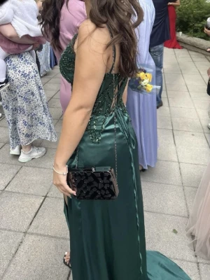 Grön långklänng med slits och snörning balklänning  - Säljer en smaragdgrön långklänning i satinliknande material med glittriga detaljer upptill, smala axelband och snygg snörning i ryggen. Klänningen har en djup slits framtill och figurnära passform. Storlek kan man påverka med tanke på att man kan spänna ryggen💕