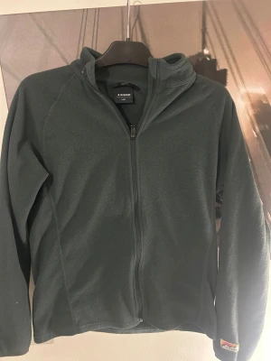 Mörkgrön fleece från Everest - Mysig mörkgrön fleece från Everest med hel dragkedja. Fleecen har ett broderat Everest-märke på ärmen och är perfekt för kalla dagar. Enkel och stilren design med lång ärm och mjukt material som håller dig varm.