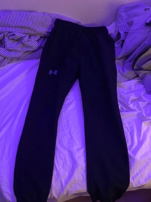 Svarta mjukisbyxor Under Armour  - Svarta mjukisbyxor från Under Armour i storlek L. Byxorna har resår och snörning i midjan, samt logga på benet. Tillverkade i 100% bomull för skön känsla. Perfekta för chill eller träning.