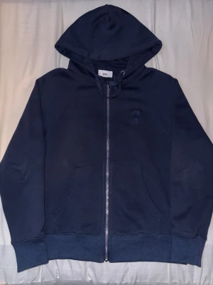 Blå Ami Paris hoodie med hjärta - Snygg marinblå hoodie från Ami Paris med det klassiska broderade hjärta-A på bröstet. Perfekt för dig som gillar stilrena streetwear-plagg med exklusiv känsla.