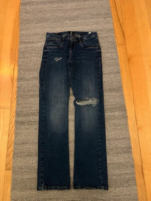 Mörkblå LTB Valerie jeans med slitningar - Snygga mörkblå jeans från LTB, modellen Valerie. Jeansen har raka ben och coola slitningar på låret och knät. Klassisk femficksdesign med kontrastsömmar och detaljerade bakfickor. Perfekta för dig som gillar en avslappnad och trendig look. Storlek 29/32