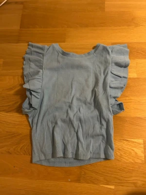 Ljusblå ribbad topp med volangärmar från Zara - Säljer en ljusblå ribbad topp med breda volangärmar. Toppen har rund hals och är croppad i modellen. Materialet känns mjukt och stretchigt, perfekt för dig som gillar en chill och snygg stil.  Den är från Zara och säljer då den ej kommer till användning. Är i strl m men kn användas som s