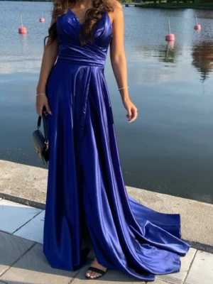 Marinblå bal/bröllops klänning i satin - Säljer en marinblå långklänning i glansigt satinmaterial. Klänningen har omlott upptill med v-ringad urringning och markerad midja. Den är ärmlös och har ett elegant, svepande fall som ger en lyxig känsla. Har använts på ett tillfälle i endast några timmar. Nypris: 3999kr