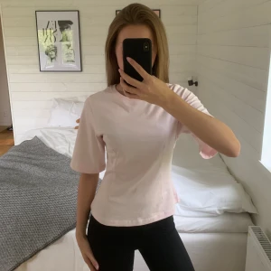 Ljusrosa t-shirt från Gina Tricot - Supersöt ljusrosa t-shirt från Gina Tricot med rund hals och lite bredare korta ärmar. Modellen är figurnära med lätt utsvängd midja och tillverkad i mjuk bomull. Säljer då den inte kommer till användning! 💋om du undrar över något så fråga bara. 