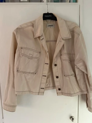 Beige overshirt från Junkyard - Säljer en beige overshirt från Junkyard i storlek L. Jackan har markerade sömmar, två stora bröstfickor med lock och knappar framtill. Tillverkad i bomull och har en croppad passform med långa ärmar och klassisk krage.