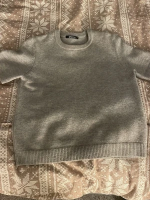 Grå stickad kortärmad tröja Gina Tricot - Säljer en enkel och stilren grå stickad tröja från Gina Tricot. Tröjan har korta ärmar, rund halsringning och ribbade muddar vid ärmslut och nederkant. Perfekt för lager på lager och funkar året runt.💞