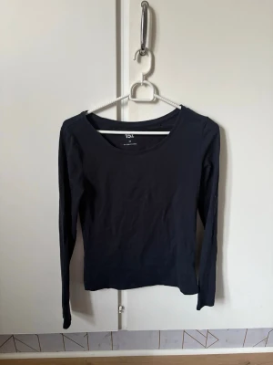 Marinblå långärmad topp från Lager 157 - En enkel marinblå långärmad topp från Lager 157 i storlek XS. Toppen har rund halsringning och är gjord i mjuk bomull med lite stretch för skön passform. Perfekt att matcha med jeans eller kjol för en clean look.