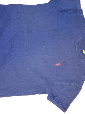 Blå t-shirt från Ralph Lauren - Snygg marinblå t-shirt från Ralph Lauren med klassisk röd logobrodyr på bröstet. T-shirten har rund hals och korta ärmar, perfekt för en chill och stilren look. Materialet är mjuk bomull som känns skönt mot huden.