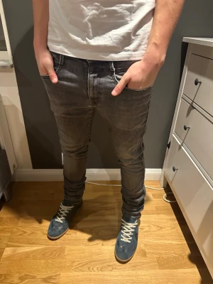 Replay Anbass grå jeans, storlek 33 - Snygga Replay Anbass jeans i grå tvätt med klassisk femficksdesign och coola detaljer på bakfickorna. Modellen är slim fit med smal passform och stretchigt material för extra komfort. Perfekt för dig som gillar en modern och stilren look.