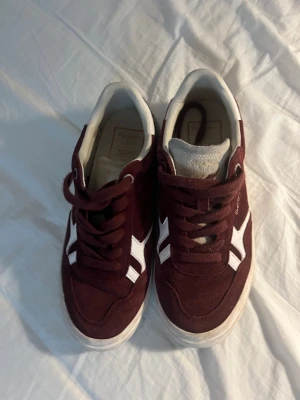 Vinröda sneakers från Pepe Jeans - Snygga vinröda sneakers från Pepe Jeans med vita och grå detaljer. Skorna har snörning, rund tå och platt sula. Ovandelen är i mocka och skinn, med vit logga på sidan och '1973' på hälen. Perfekt för dig som gillar klassisk streetstil.